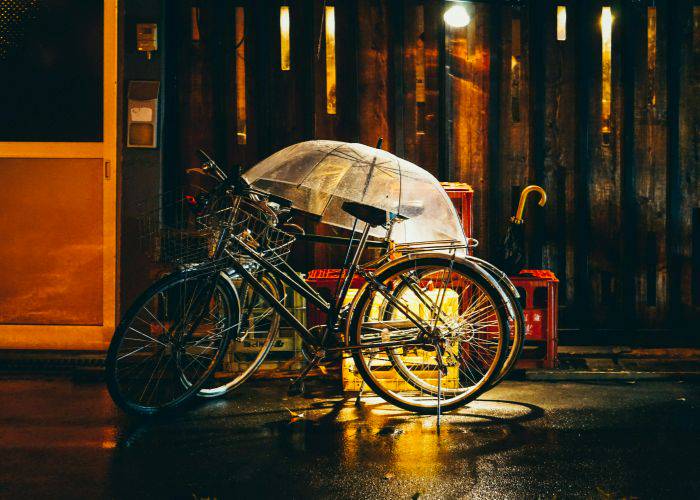 Two bicycles left out in the rain, covered by a see-through umbrella.